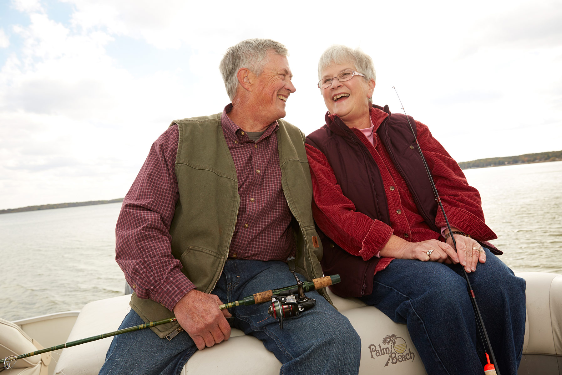 A senior couple holding fishing poles, sitting on the back of a pontoon.