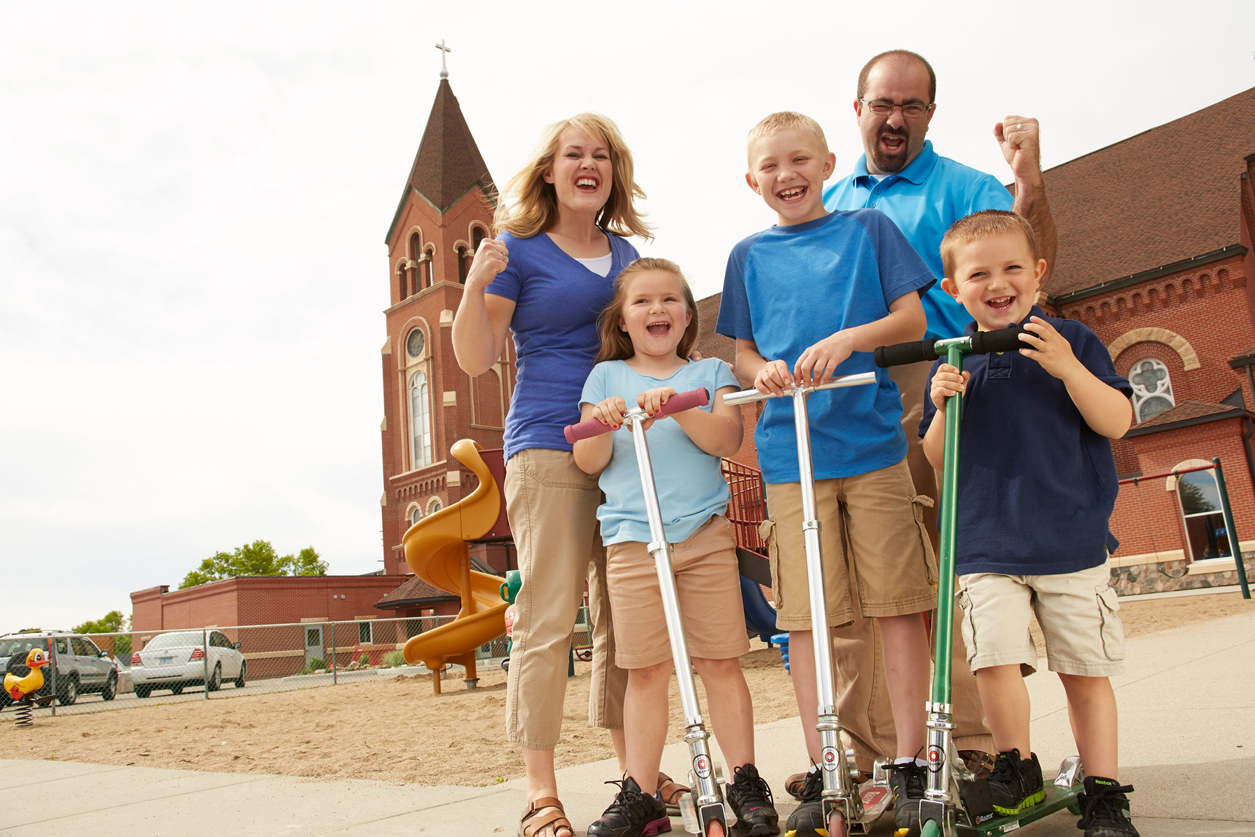 A family of 5 riding scooters at the church playground.