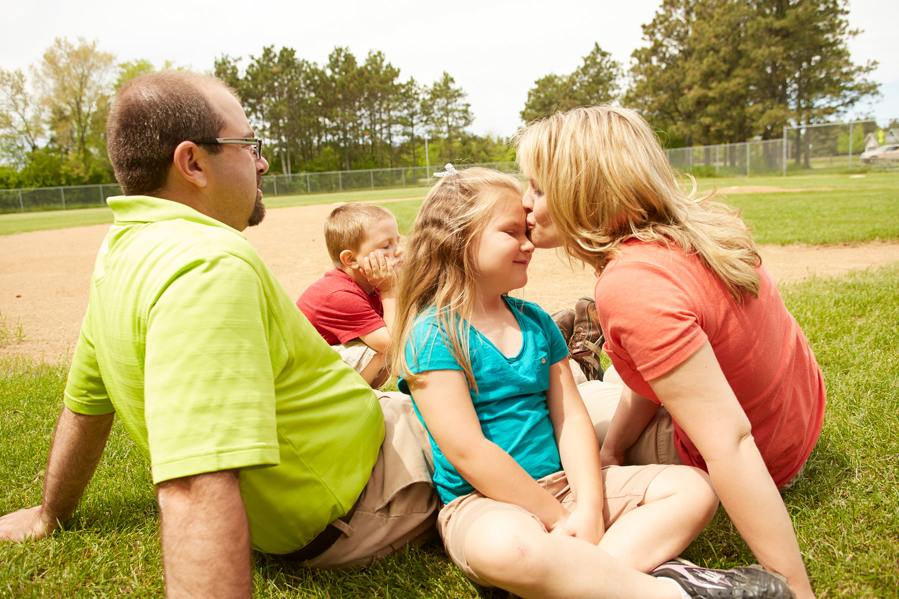 A mother kissing her daughters forehead with father and son close by.