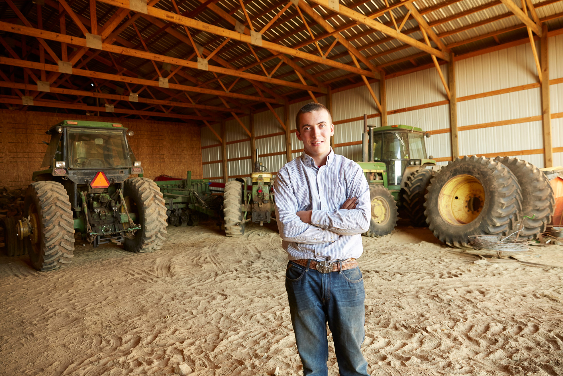 A young gentleman standing in front of his tractors in their shed.