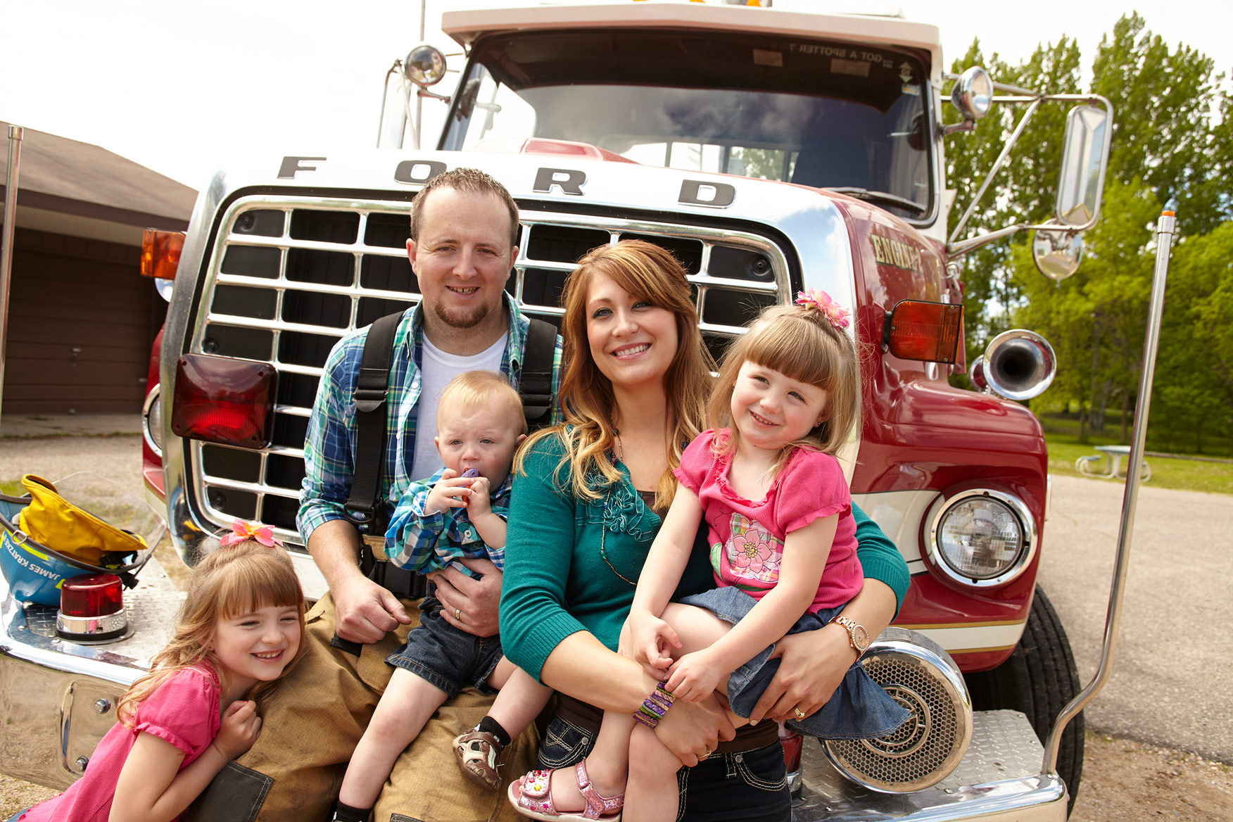 A firefighter father and his wife and 3 children in front of an old, red firetruck.